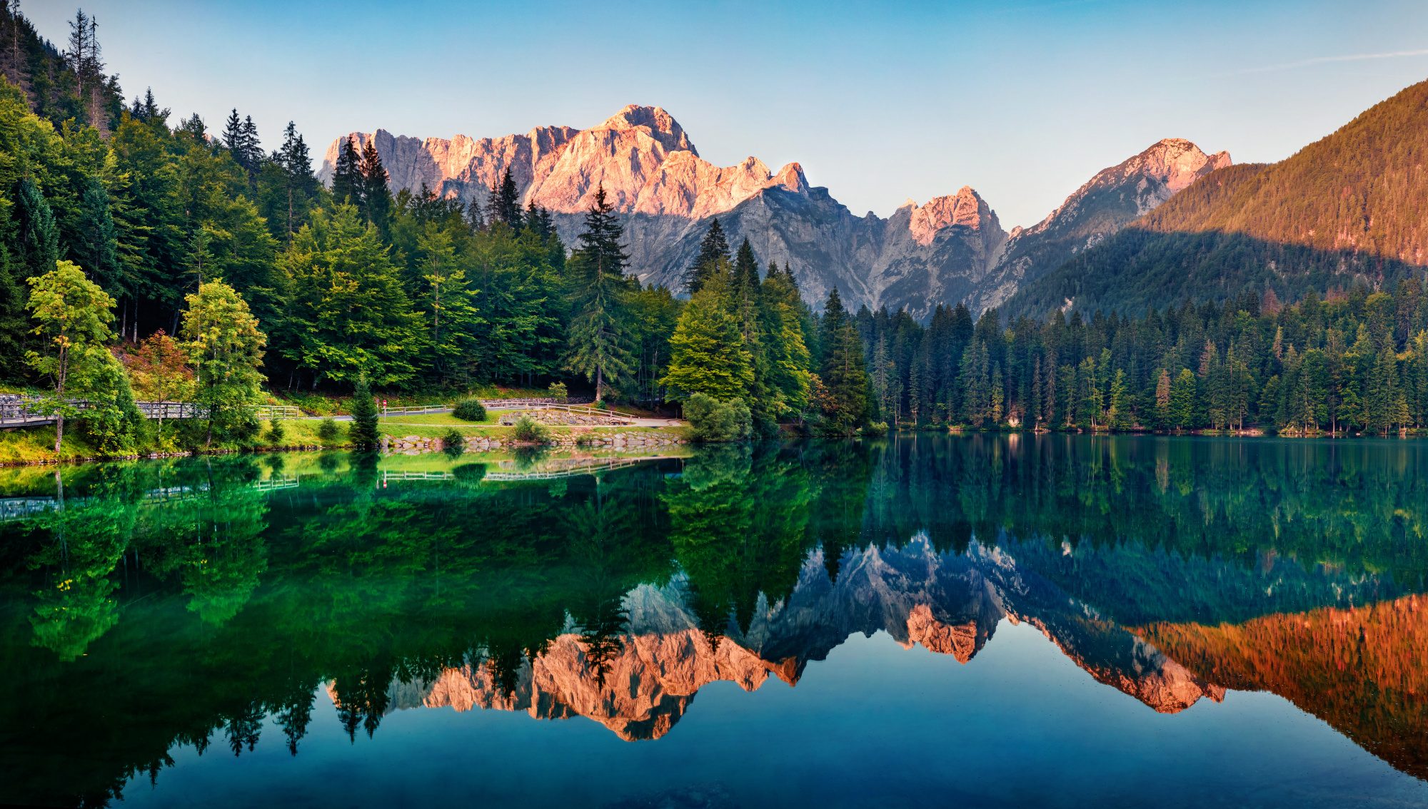 Photomural Calm Morning View Of Fusine Lake. Colorful Summer Sunrise In Julian Alps With Mangart Peak On Background, Province Of Udine, Italy, Europe. Beauty Of Nature Concept Background.